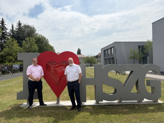 : Prof. Dr.-Ing. Alexander Kratzsch und Prof. Dr.-Ing. Sascha Müller-Feuerstein vor dem I Love HSZG Logo auf dem Campus