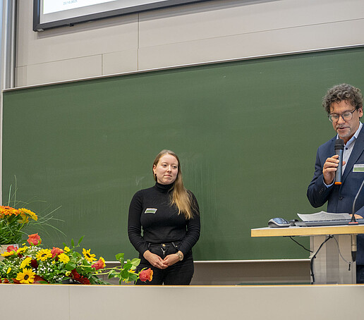 Prof. Zips hält eine Laudatio auf die Al-Makhawi-Preisträgerin, die lächelnd daneben steht.