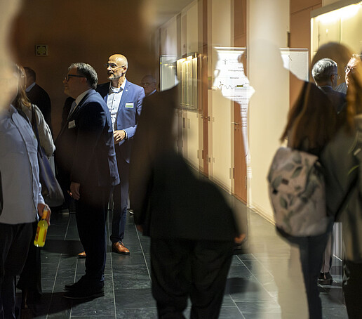 Auf einem dunklen Gang, der an den Wänden beleuchtet ist, laufen Gäste entlang und schauen sich Exponate an.
