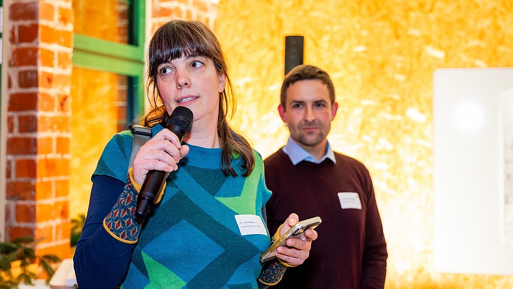 Julia Gabler spricht in ein Mikrofon, daneben steht ein Mitarbeiter.
