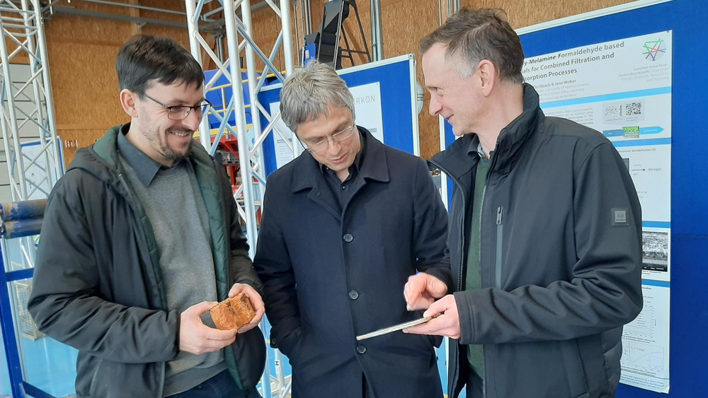 Drei Männer schauen sich in der Lander-Halle Materialien zur nachhaltig produzierten Windturbine an.