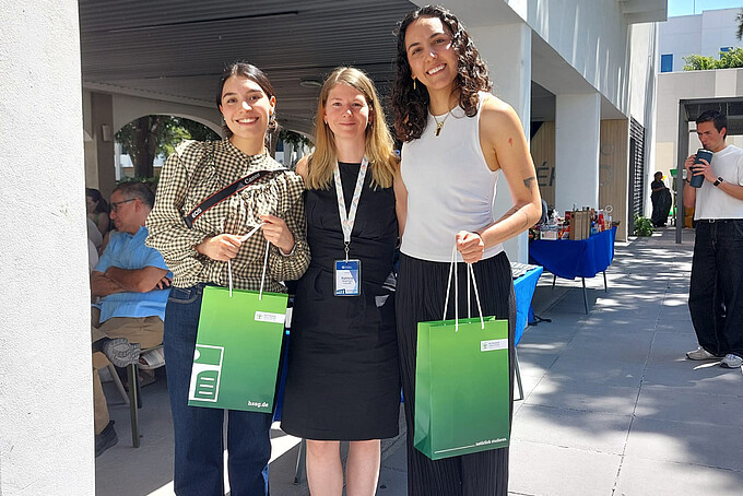 Zwei Frauen halten eine HSZG-Geschenketüte in der Hand, in der Mitte steht Patricia Stange.