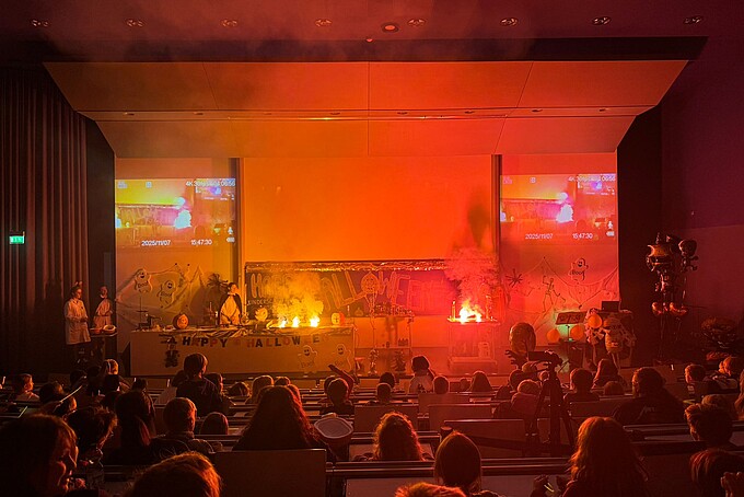 Die Bühne leuchtet in roter Farbe. Das Kinderpublikum schaut staunend in Richtung Bühne.