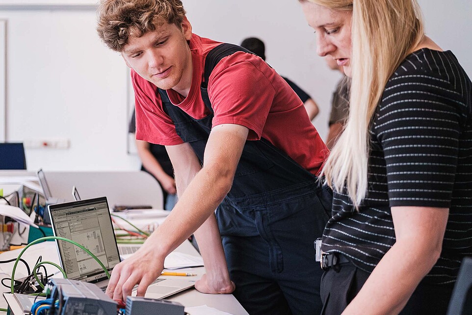 Die KIA-Beauftragte lässt sich an einem Versuchsstand von einem Mitarbeiter eine Anlage erklären.