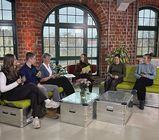 Teilnehmende Studierende und die Prorektorin Bildung sitzen mit der Moderatorin im TV-Studio auf grünen Sofas und beantworten Interviewfragen.